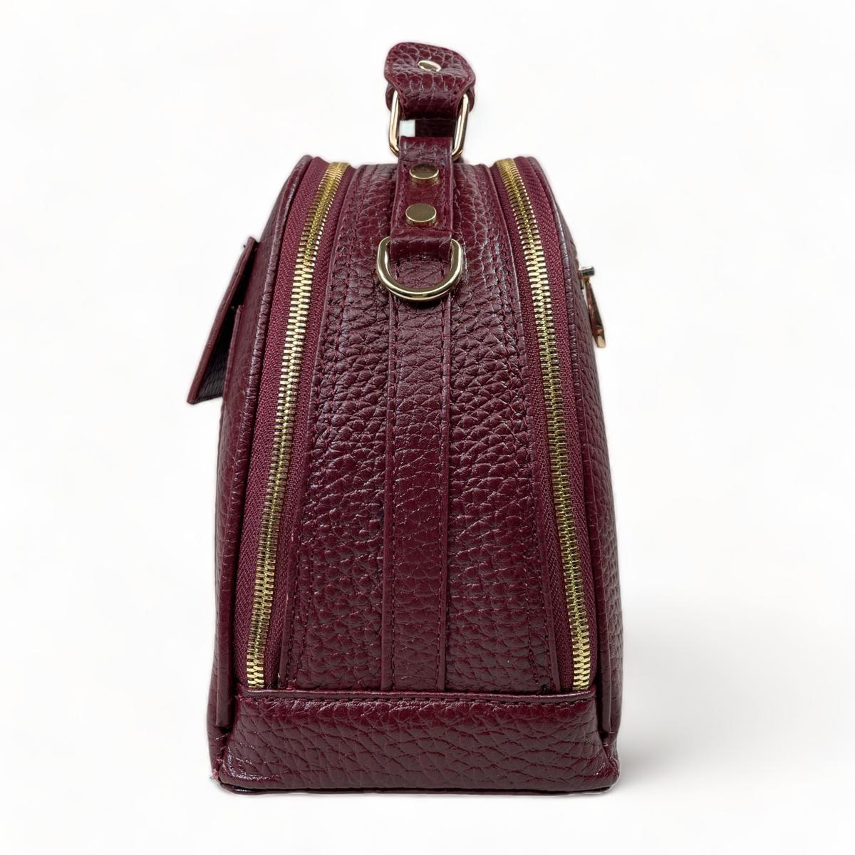Side profile of dark red leather satchel showing dual zip compartments and D-ring for detachable strap
