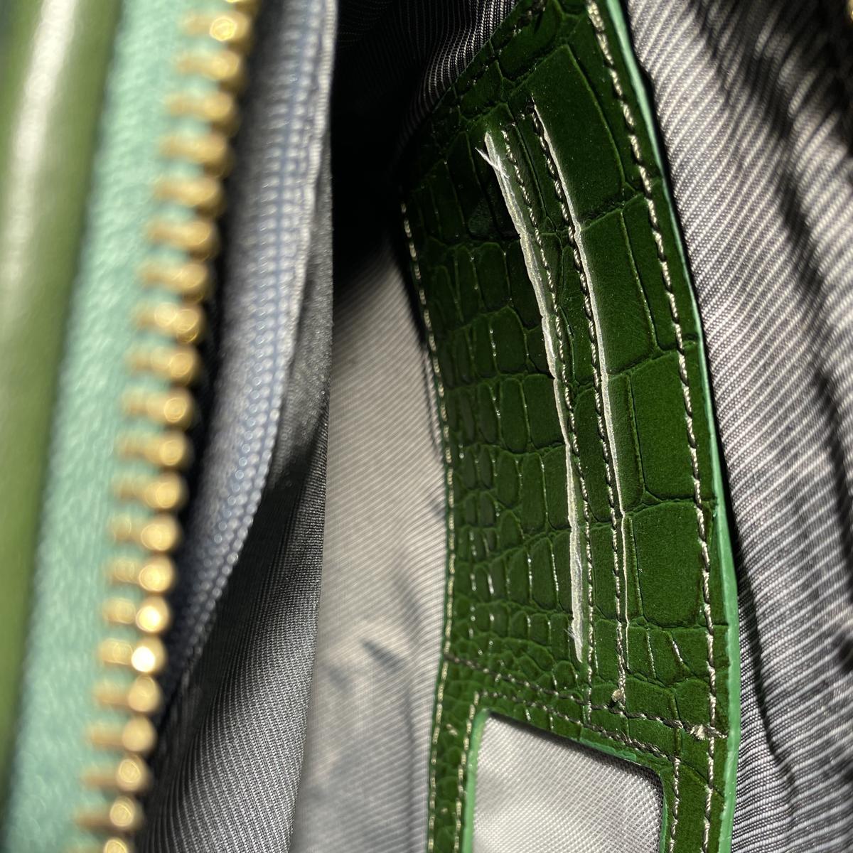 Close-up of green leather clutch interior showing zip compartments and card pockets