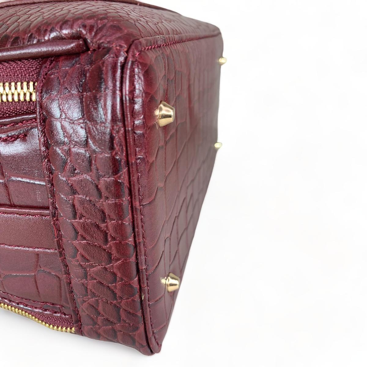 Red leather handbag bottom profile displaying shoulder strap and compartments