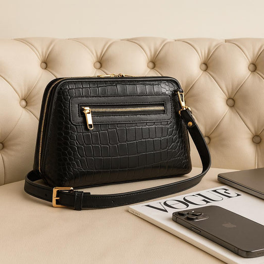 Black crocodile-patterned handbag on a beige surface with a magazine and phone.