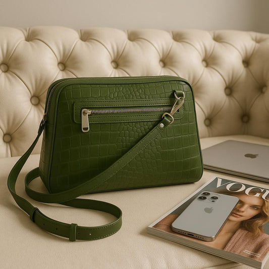 Green crocodile-patterned handbag on a beige surface with a magazine and phone.