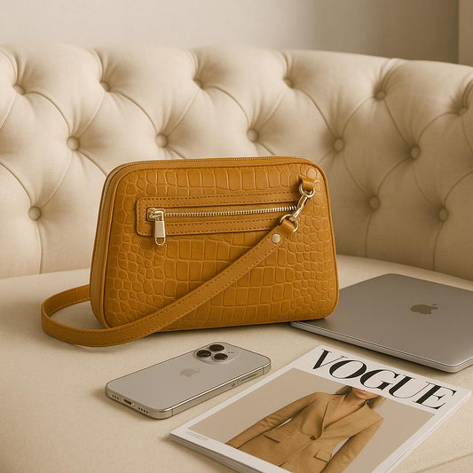 Brown crocodile-patterned handbag on a beige couch with a phone, magazine, and laptop.