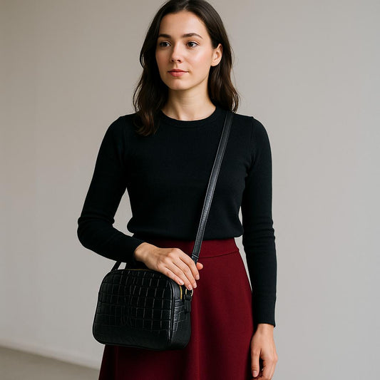 Woman holding a black handbag against a plain background