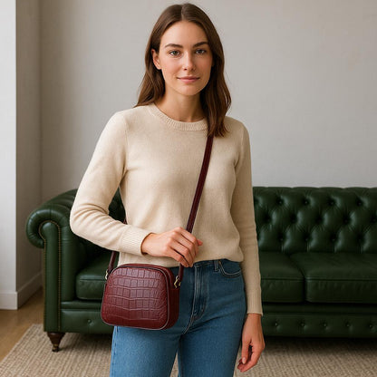 Woman holding a maroon handbag in a room with a green couch.