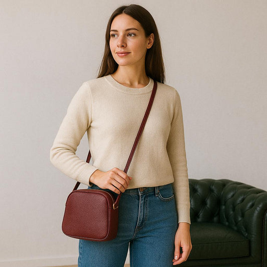 Model holding dark red leather satchel by the handle in a home setting