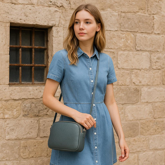 Woman in a denim dress holding a green handbag against a stone wall.